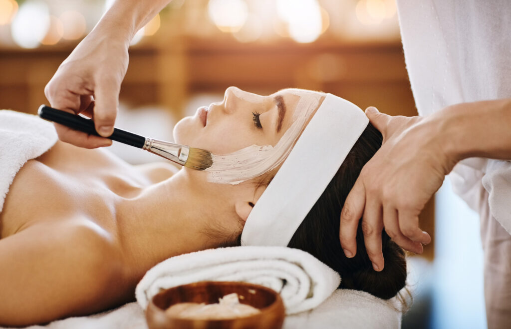 Woman, spa and face mask with brush for application, pamper weekend and skincare wellness with client. Facialist, treatment and skin rejuvenation or pore tightening, relaxation and facial with people